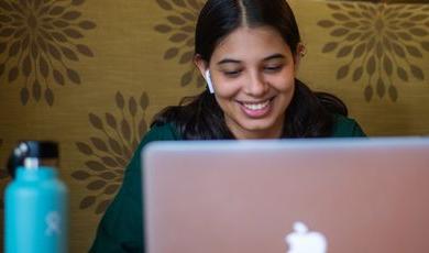 Woman is smiling while looking down at her laptop 