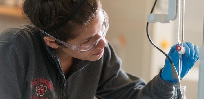 一名学生戴着橡胶手套和安全眼镜在化学实验室使用设备