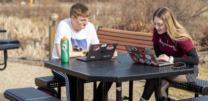 两个学生坐在户外的桌子上，打开笔记本电脑学习